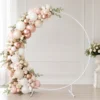 Arche ronde en métal blanc décorée avec ballons et fleurs Arche ronde en métal blanc décorée avec ballons rose poudré, nude, blanc et rose gold, fleurs claires et feuillage dans un décor événementiel chic.