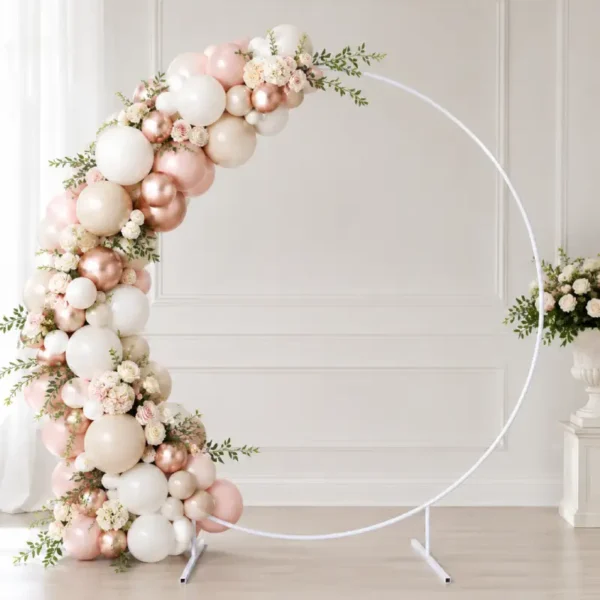 Arche ronde en métal blanc décorée avec ballons et fleurs Arche ronde en métal blanc décorée avec ballons rose poudré, nude, blanc et rose gold, fleurs claires et feuillage dans un décor événementiel chic.