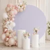 Backdrop rond blanc décoré avec ballons, fleurs et colonnes blanches Backdrop rond blanc sur pied décoré avec ballons rose poudré, blanc et nude, fleurs claires et trois colonnes blanches devant.