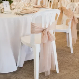 Chaise blanche de réception avec nœud en tissu au dos dans une salle décorée pour un événement.