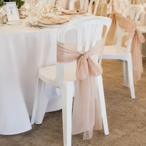 Chaise blanche de réception avec nœud en tissu au dos dans une salle décorée pour un événement.