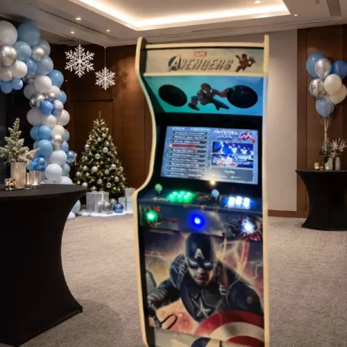 Borne d’arcade super-héros en location, placée dans une salle décorée pour un arbre de Noël d’entreprise avec ballons bleu ciel, blanc et argent, flocons de neige et espace événementiel.