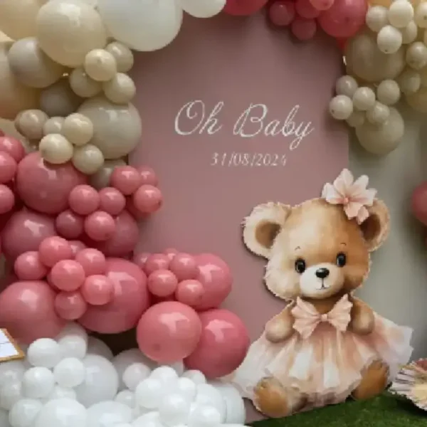 Décoration événementielle enfant avec ourson décoratif en PVC devant un panneau rose et une arche de ballons rose, blanc et beige.