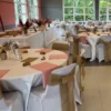 Salle de réception avec housses de chaises blanches et rubans noués en toile de jute autour des dossiers.