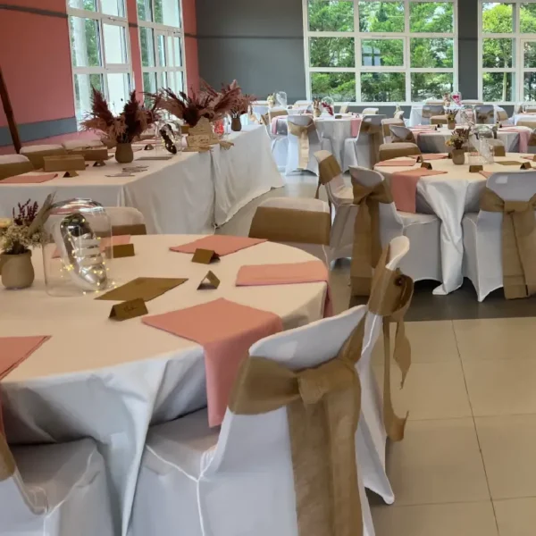 Salle de réception avec housses de chaises blanches et rubans noués en toile de jute autour des dossiers.
