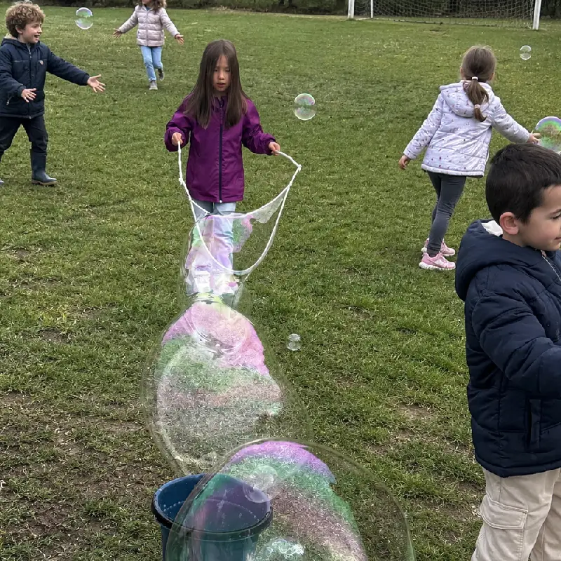 Enfants découvrant une animation de bulles géantes sur une pelouse.
