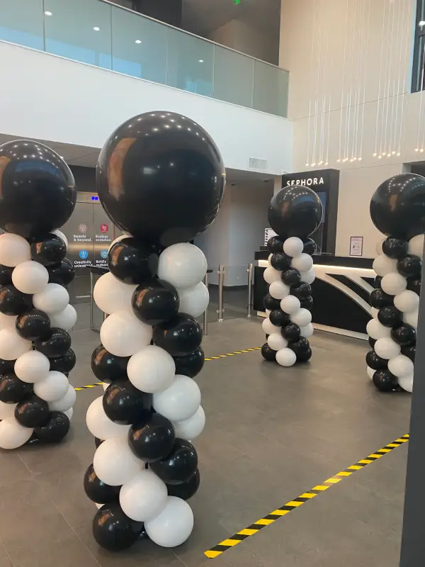 Quatre colonnes de ballons noir et blanc installées dans un espace d’accueil moderne devant un comptoir Sephora.
