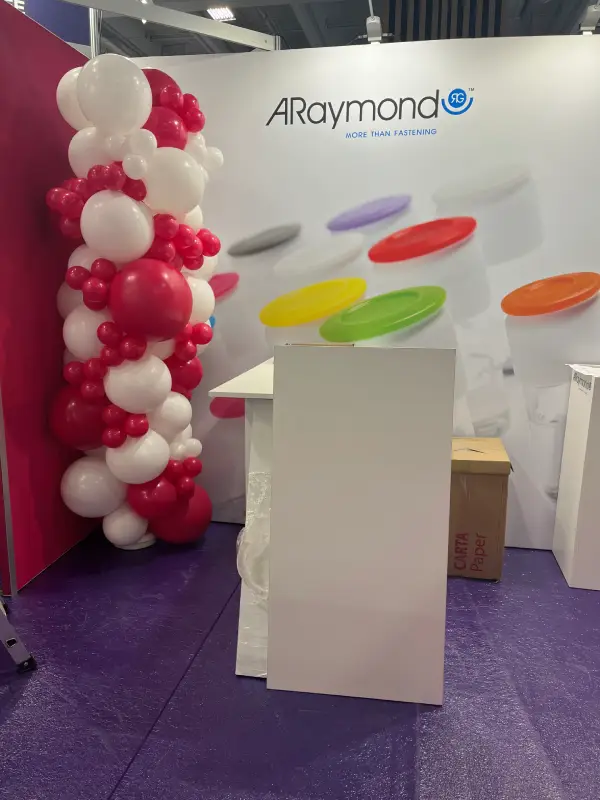 Colonne organique de ballons roses et blancs installée sur un stand d’exposition professionnel.