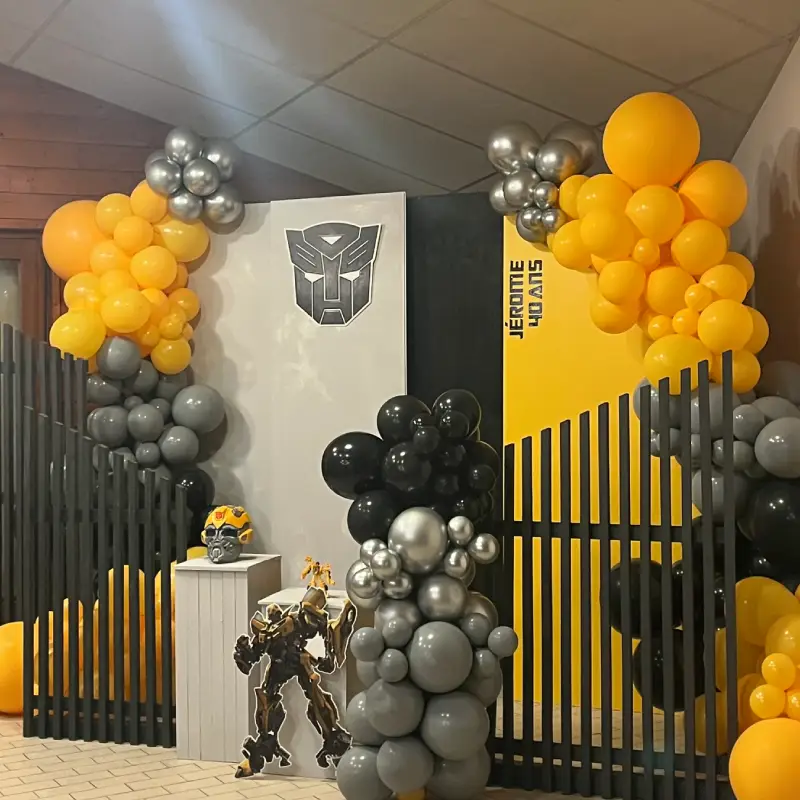 Décor d’anniversaire Transformers avec arche organique en ballons jaunes, gris et noirs et mise en scène personnalisée.