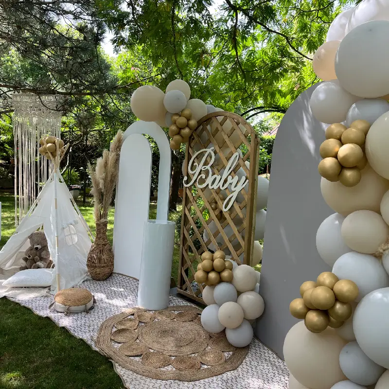 Décoration de baby shower bohème en extérieur avec ballons blancs et dorés, tipi, panneaux décoratifs et mise en scène naturelle.