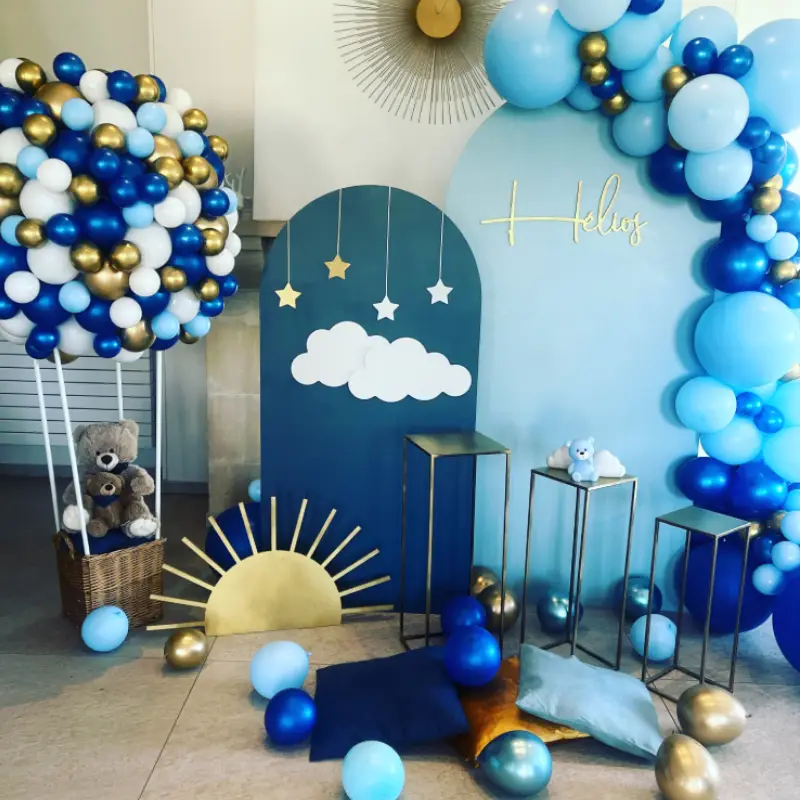 Décoration de baptême pour Hélos avec panneaux personnalisés, arche de ballons bleus et or et montgolfière en ballons.